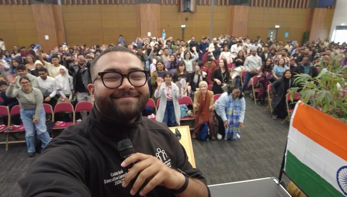 Murtuza taking a selfie on stage in front of a waving audience of international students
